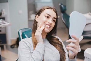 Smiling woman in dental chair examining her teeth in a mirror, showcasing the positive experience of dental care at Trail Ridge Dental.